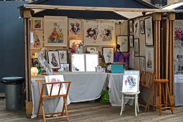 A craft stall displaying art prints and cards beneath an awning.
