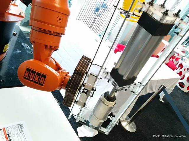 An orange industrial robot beside a 3D printing apparatus at a London exhibition.